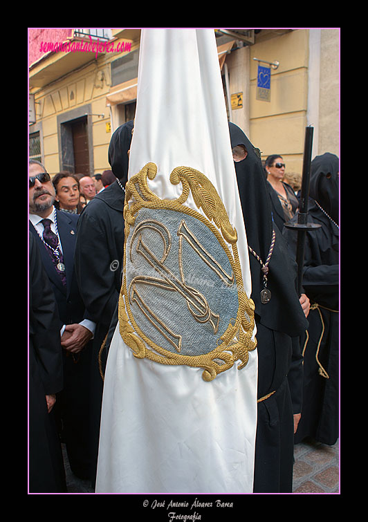 Nazareno portando la Bandera de Devotos de la Hermandad de Nuestra Señora de Amor y Sacrificio