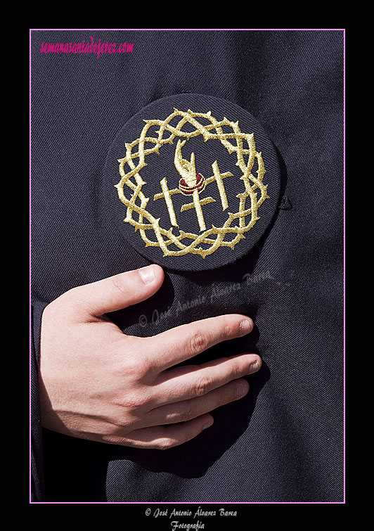 Escudo de la Hermandad sobre el antifaz de los nazarenos de la Hermandad del Santísimo Cristo del Perdón