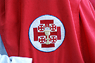 Escudo sobre el antifaz de los nazarenos de la Hermandad de la Sagrada Cena