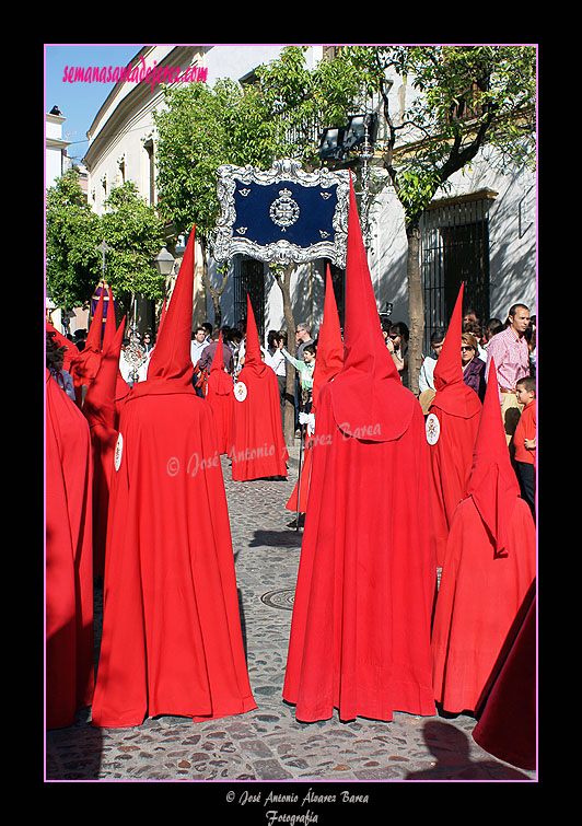 Nazareno portando el Banderín conmemorativo del XXV aniversario de la reorganización de la Hermandad de la Sagrada Cena