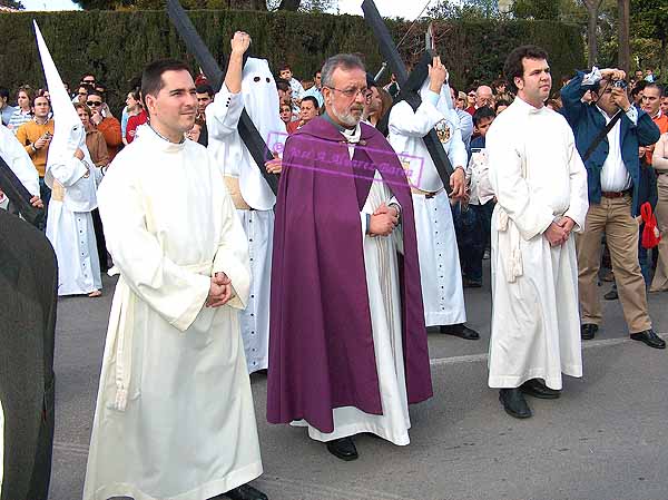 Preste acompañado de acolitos tras el Paso de Misterio de la Hermandad de la Clemencia