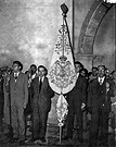 Año 1956, Domingo de Ramos. La Hermandad de la Cena en la puerta de la Parroquia de San Marcos - su sede canónica - espera el paso de la Cofradía de la Borriquita. El estandarte de la Hermandad es blanco y lleva bordado el escudo original (las varas son propiedad de la Sacramental de Santiago) (Fondo Documental Fernández Lira)